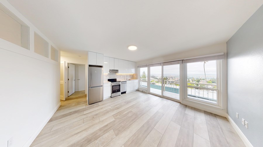 A spacious room with wooden flooring and a kitchen area in the background.